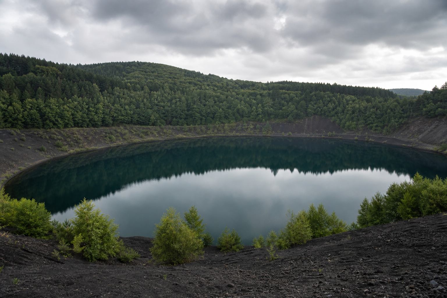 Tiefblaues Maar mit Waldrand und ruhiger Wasserfläche in der Vulkaneifel